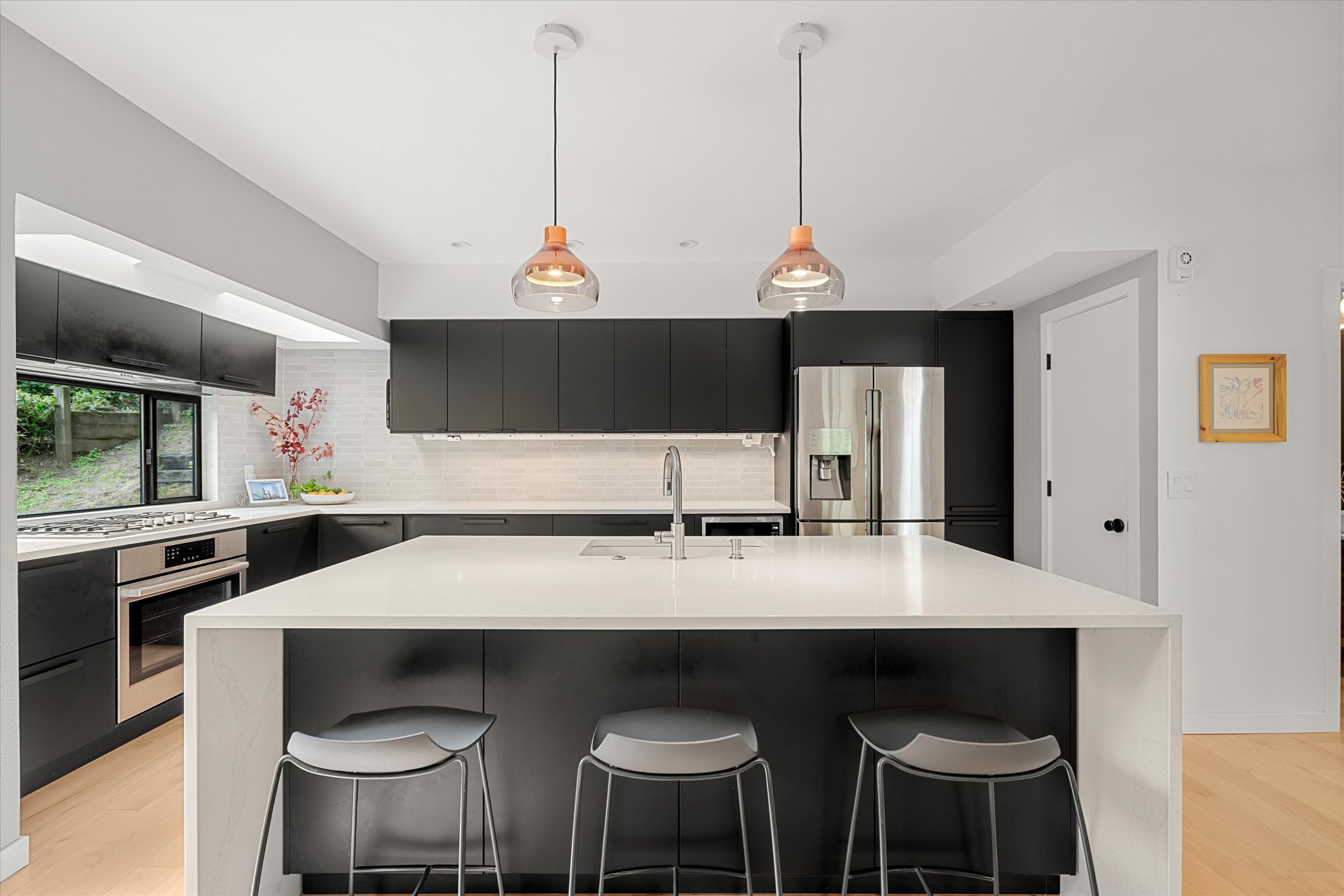 The kitchen island with dark matte cabinetry and copper pendant lights
